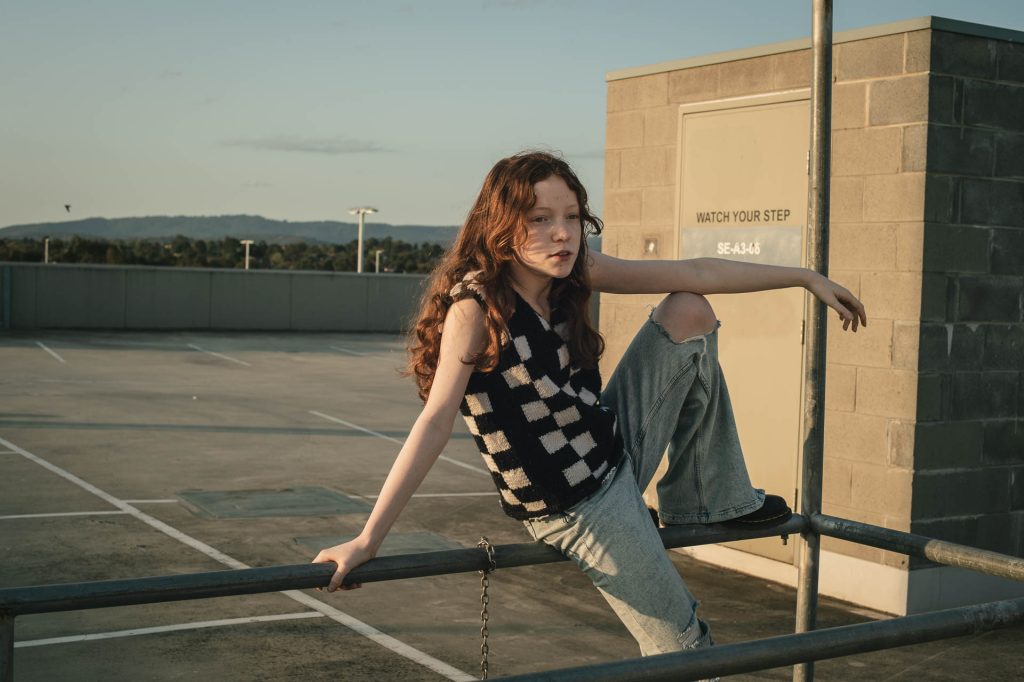 portrait of a girl sitting in a shopping centre car park at sunset