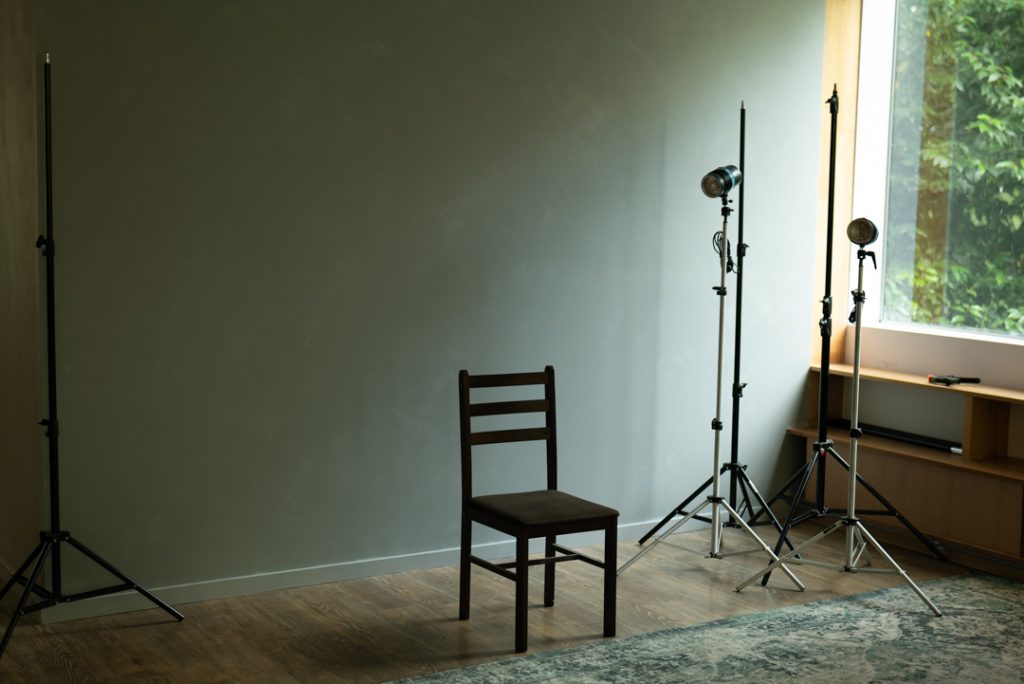 a wooden chair sitting in front of a large wall with tripods and vintage studio lights off to the side in a purpose built portrait studio in Olinda