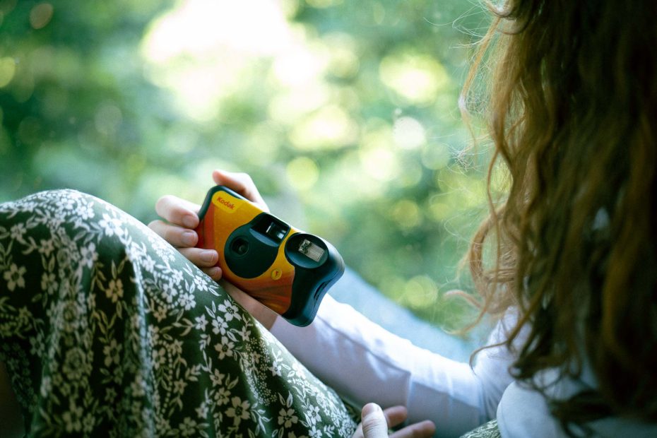 photo of a girl sitting in a window holding onto a Kodak disposable camera